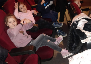 Dziewczynki i chłopiec siedzą na fotelach w kinie i czekają na początek filmu.