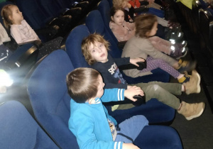 Dzieci siedzą na fotelach w kinie i czekają na początek filmu.