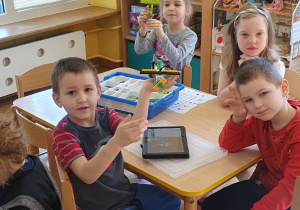 Dzieci siedzą przy stoliku i prezentują zbudowane budowle z klocków Lego na zajęciach z robotyki i programowania.