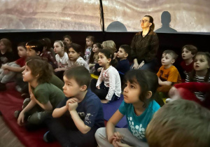 Dzieci siedzą na materacach i odbywają wycieczkę w kosmos za pomocą specjalnego pokazu w mobilnym planetarium w wielkim balonowym namiocie.