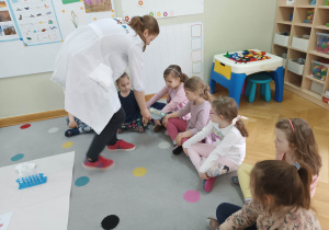 Dzieci siedzą na dywanie, a prowadząca warsztaty chemiczne LABOLO prezentując im wynik przeprowadzonego doświadczenia.