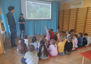 Dzieci siedzą na materacach i oglądają prezentację multimedialną nt. parków i terenów zielonych w mieście.