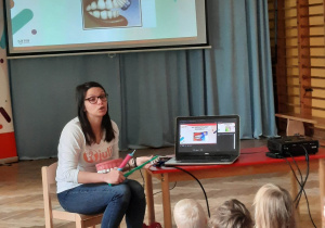 Dzieci siedzą na materacach i oglądają prezentację nt. sposobu szczotkowania zębów.