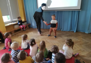 Dzieci siedzą na materacach i oglądają prezentację nt. kina niemego, a prowadzący warsztaty Szkatułki odrywa scenkę z chłopcem.