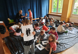 Dzieci siedzą na podłodze na folii i przyklejają czarno-białe obrazki do kartek i tworzą z nich pracę.