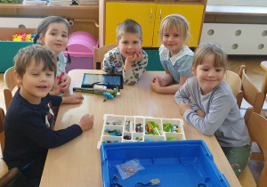 Dzieci siedzą przy stoliku prezentując ułożoną budowlę z klocków LEGO na warsztatach z robotyki.