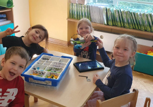 Dzieci siedzą przy stoliku prezentując ułożoną budowlę z klocków LEGO na warsztatach z robotyki.