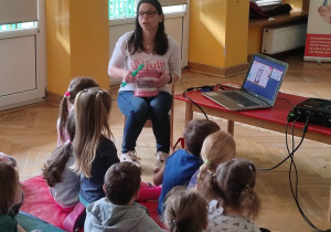 Dzieci siedzą na materacach, a prowadząca warsztaty stomatologiczne pokazuje im model ludzkiej szczęki i jak o nią dbać.