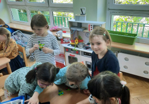 Dzieci siedzą przy stolikach i układają robociki z klocków LEGO wg. instrukcji wyświetlanej na tablecie na warsztatach z robotyki i programowania.