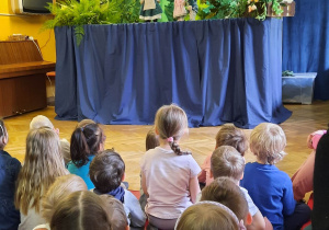 Dzieci siedzą na materacach i oglądają teatrzyk kukiełkowy pt. "Kwiat paproci".