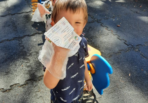 Chłopiec przez torebkę foliową trzyma w ręce papierek, który podniósł z ziemi.