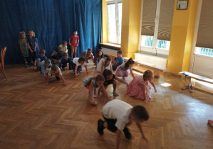 Dzieci w pozycji na czworakach przemieszczają się z jednego końca sali do drugiego.
