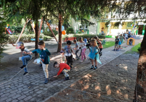 Grupa chłopców i dziewczynek próbuje przejść na drugą stronę rozpostartej między drzewami pajęczynki.