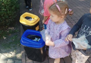 Dziewczynka i chłopiec stoją przy koszach do recyklingu.