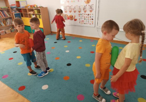 Dzieci stoją w parach twarzami do siebie, pomiędzy brzuszkami trzymają baloniki i starają się tańczy tak, aby im one nie spadły na podłogę.
