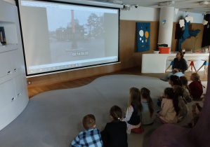 Dzieci oglądają prezentację na temat ruchu ulicznego w Warszawie sprzed stu lat.