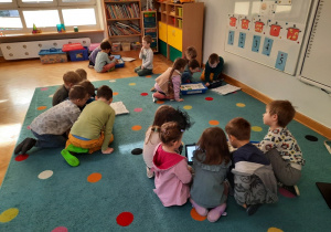 Dzieci podzielone na cztero i pięcio osobowe zespoły odczytują instrukcję na tabletach.