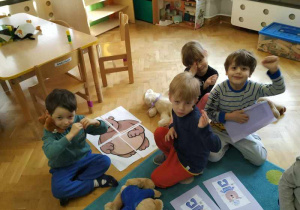 Dziewczynka i trzech chłopców siedzą razem w grupie i prezentują ułożony obrazek misia.