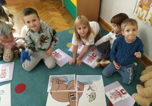 Dwie dziewczynki i dwóch chłopców siedzą razem w grupie i prezentują ułożony obrazek misia.