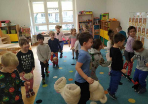 Dzieci tańczą na dywanie z misiami między kolanami.