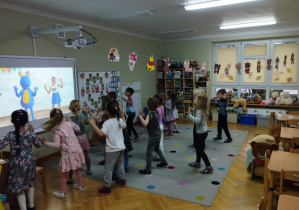 Przedszkolaki tańczą do piosenki wyświetlanej na tablicy multimedialnej.