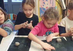 Trzy dziewczynki i chłopiec formują kule z gliny.