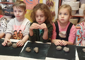 Trzy dziewczynki i dwóch chłopców siedzą przy stole i dzielą kawałek gliny na dwie połowy.