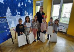 Dwóch chłopców oraz cztery dziewczynki pozują wraz z prowadzącą do zdjęcię po odebraniu dyplomów oraz nagród za udział w konkursie.