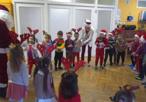 Przedszkolaki z grupy III stoją w kole i naśladują za Mikołajem przekazywanie z rąk do rąk mikołajowego worka.