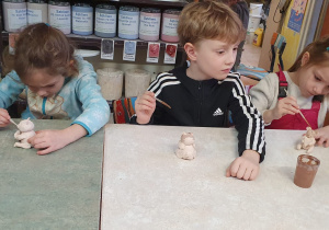 Trzy dziewczynki i chłopiec pokrywają ulepioną przez siebie figurkę misia farbą w kolorze brązowym.