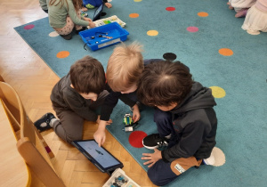 Trzej chłopcy wpatrzeni w tablet uzgadniają czy ich robot jest już gotowy do użycia.