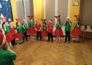 Dzieci stoją w półkolu śpiewając piosenkę o Mikołaju, gestykulując jej treść.