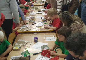 Rodzice pomagają dzieciom odrysować świąteczne wzory wewnątrz ramek.