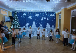Cała grupa stoi w półkolu, dzieci w ręku trzymając latarki wykonują taniec światełek.