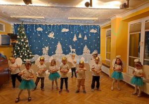 Maluszki stoją w szachownicy na środku sali, za pomocą gestów i śpiewu wykonują świąteczną piosenkę.