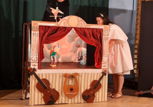 Artystki poruszają marionetkami, które umieszone są na scenie przypominającą tę w operze.