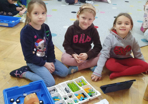 Trzy dziewczynki siedzą przed tabletem i zaczynają budować swojego robota z klocków.