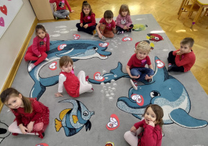 Dzieci siedzą na dywanie, przed sobą mają złożone i naklejone na serduszka części układanki.