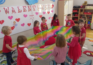 Dzieci trzymają w rękach kolorową chustę, na której leży pluszowe serce.