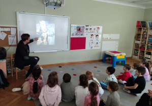Zaproszony rodzic opowiada przedszkolakom o pracy astronautów na podstawie zdjęć wyświetlonych na tablicy multimedialnej.