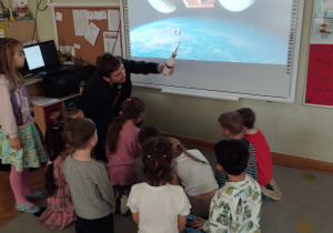 Zaproszony gość opowiada dzieciom o kosmosie pokazując jego zdjęcia na tablicy interaktywnej.