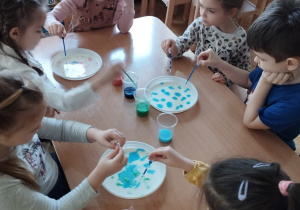 Dzieci malują rozwodnionymi farbami powierzchnię plastikowych talerzyków, zakrapiając ją różnymi kolorami.
