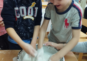 Dwaj chłopcy mieszają mąkę z wodą tworząc masę sensoryczną.