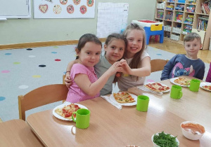 Cztery dziewczynki i chłopiec siedzą przy stoliku, przed sobą mają gotowe do degustacji pizze.
