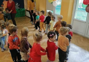 Dzieci ustawione w pociągu wraz z nauczycielką i pomocą nauczyciela tańczą do piosenki na balu Jesieni.