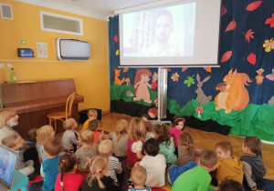 Dzieci siedzą na materacach na sali gimnastycznej podczas spotkania autorskiego z Panem Łukaszem Tartasem o wierszykach o kocie Amadeuszu.