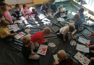 Dzieci siedzą w kole na folii i farbami malują prace.