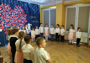 Przedszkolaki stoją w półkolu i śpewają piosenkę dla dziadków.