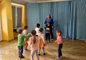 Dzieci zwrócone w kierunku prowadzącej tańczą do piosenki.