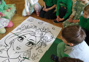 Pięcioro chłopców i dwie dziewczynki siedzą wokół ułożonego obrazka prezentującego Panią Wiosnę.